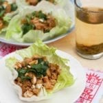 A Chinese chicken lettuce cup topped with cashews and cilantro on a white plate.
