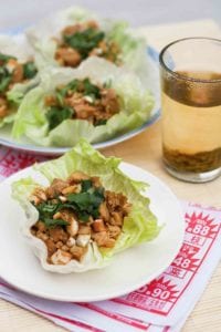 A Chinese chicken lettuce cup topped with cashews and cilantro on a white plate.