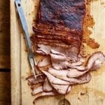 A partially sliced smoked coffee brisket on a wooden cutting board with a meat fork resting beside it.