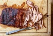 A partially sliced smoked coffee brisket on a wooden cutting board with a meat fork resting beside it.