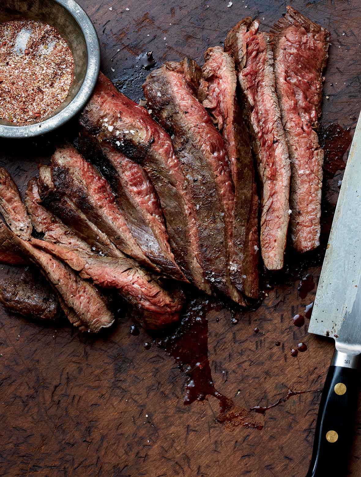 Cheap Cuts: A sliced grilled flank steak with a bowl of seasoning mix and a knife on the side.