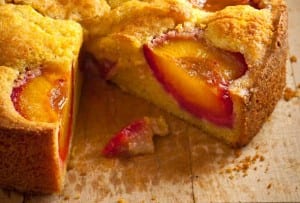 A round polenta plum cake on a wooden table with one slice cut from it.