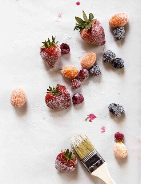 Various berries and fruit dipped in sugar on a sheet of parchment.