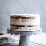 A double layer cake on a cake stand frosted in white chocolate-cream cheese frosting