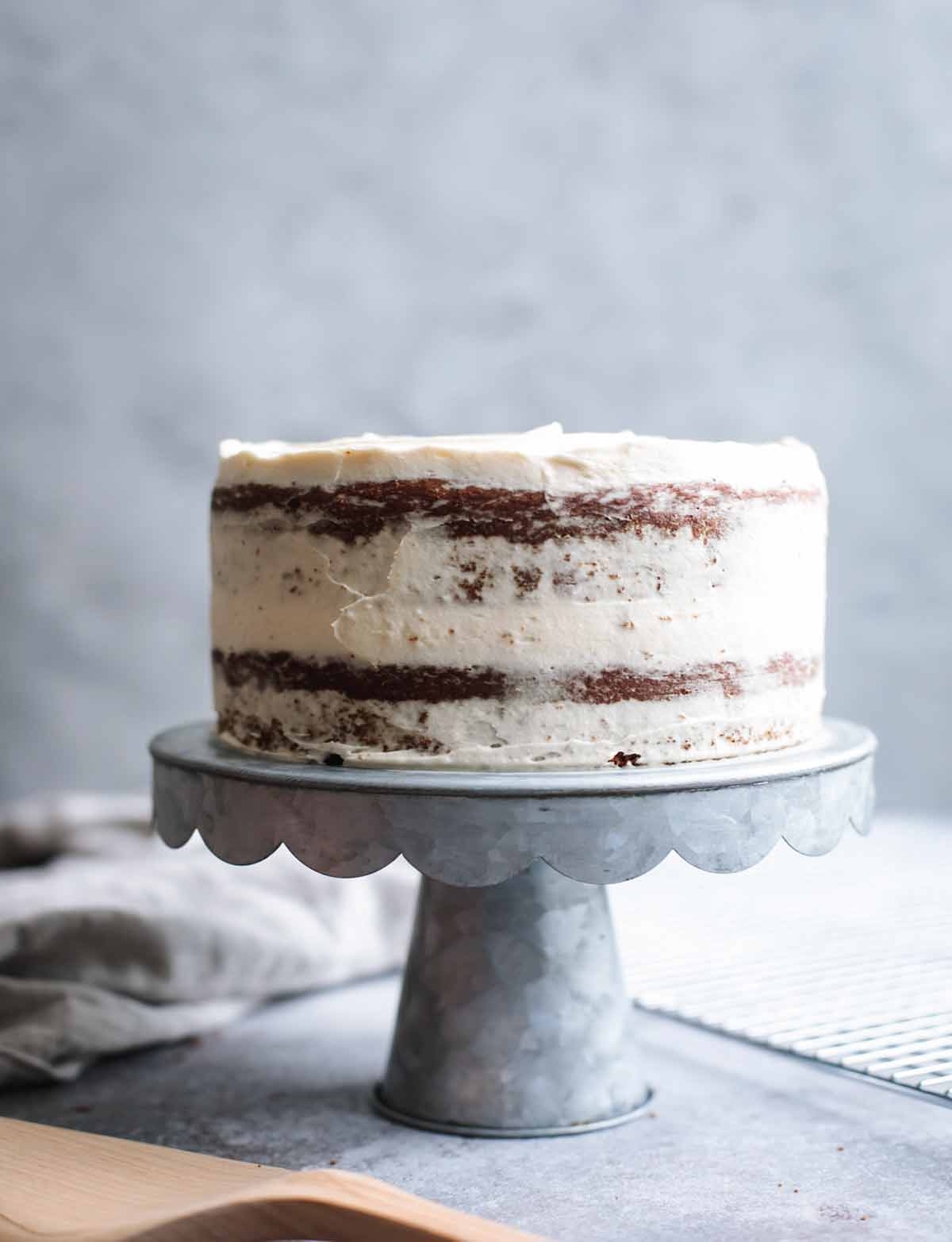 A double layer cake on a cake stand frosted in white chocolate-cream cheese frosting