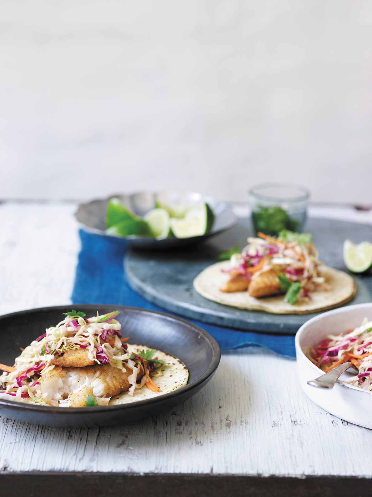 A plate with a fish taco topped with creamy chipotle cabbage slow with a bowl of slaw beside it.