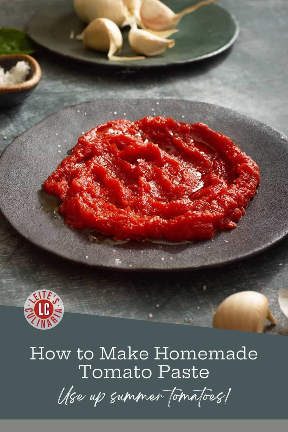 Rich, homemade tomato paste on a dark plate with garlic cloves in the background, with text that reads "How to Make Homemade Tomato Paste."