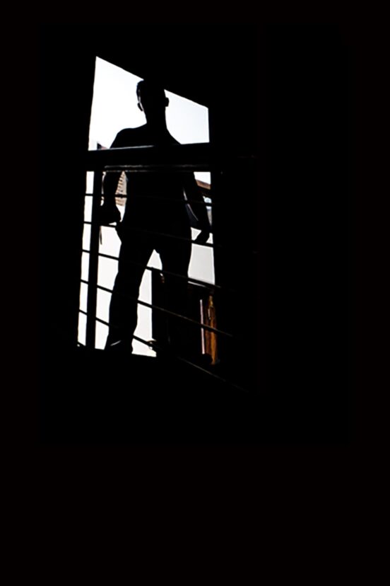A man silhouetted at the top of a dark stairway.