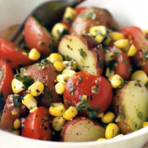 Potato, corn, and tomato salad with basil dressing in a white bowl with a fork.