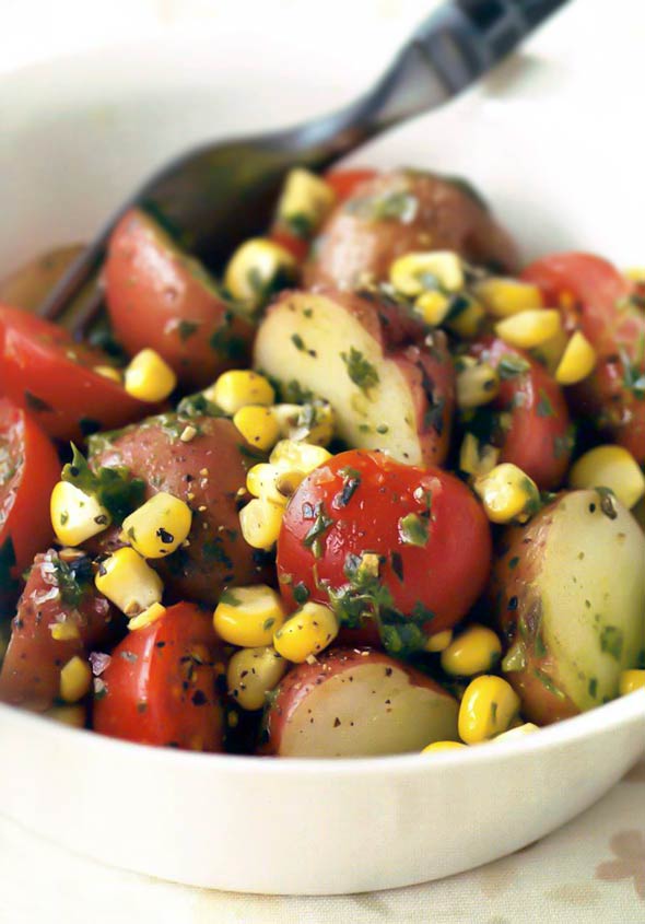 Potato, corn, and tomato salad with basil dressing in a white bowl with a fork.