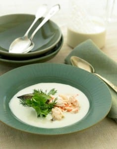 Portuguese white gazpacho with crab salad in a green soup bowl with bowls and flatware in the background.