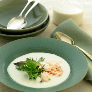 Portuguese white gazpacho with crab salad in a green soup bowl with bowls and flatware in the background.
