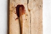A wooden spoon that's been dipped in cajeta, laying on a wooden cutting board with drips of cajeta.