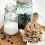 A stack of Neiman Marcus cookies on wooden board with a bottle of milk and a jar of chocolate chips.