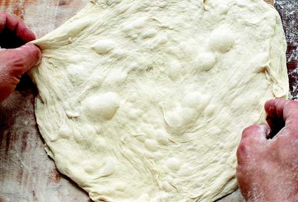 Hands stretching out pizza dough.