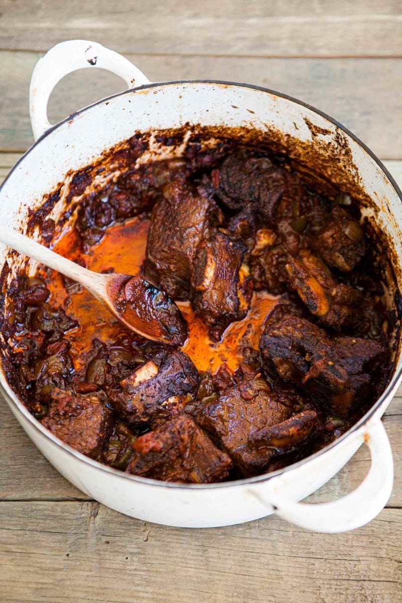 A white enamel pot with pieces of beef short ribs with chile rub and a wooden spoon.