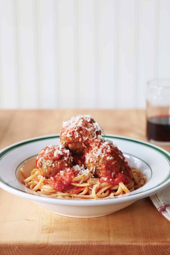 Three classic beef meatballs piled on pasta in a white and green bowl an finished with Parmesan.