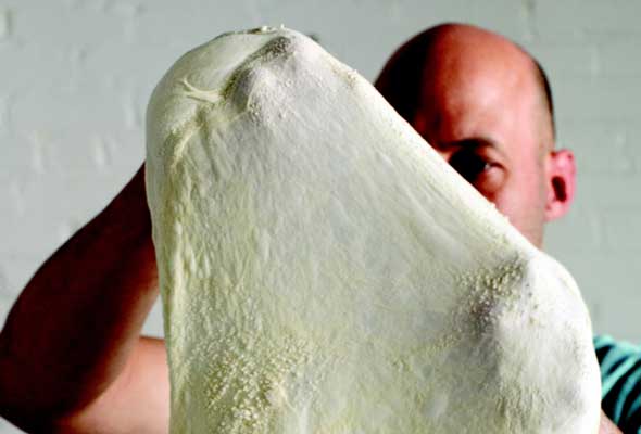 Final Stretching of Pizza Dough with man standing behind it.