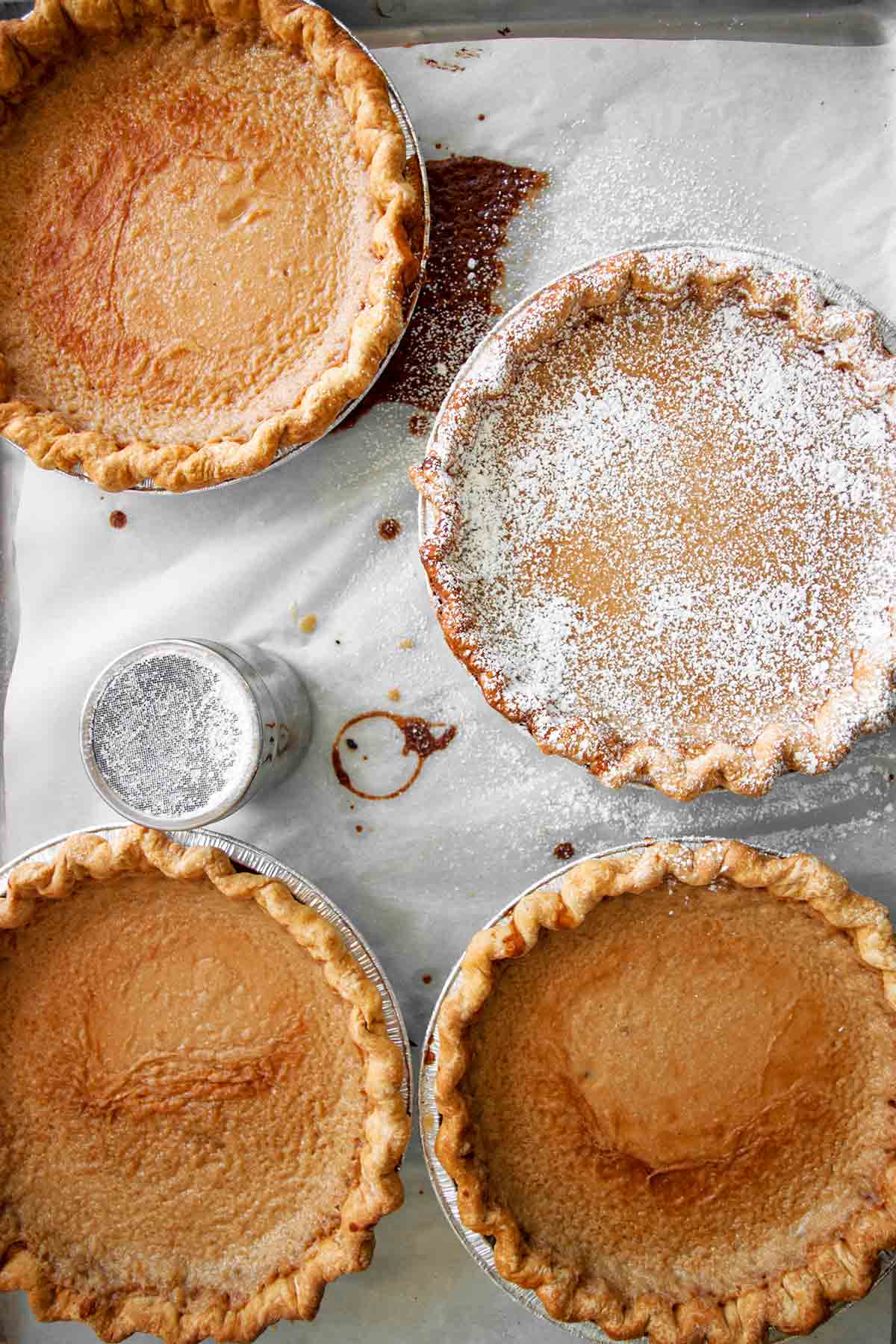 Four Hoosier sugar cream pies, one dusted with confectioners' sugar on a sheet of parchment.