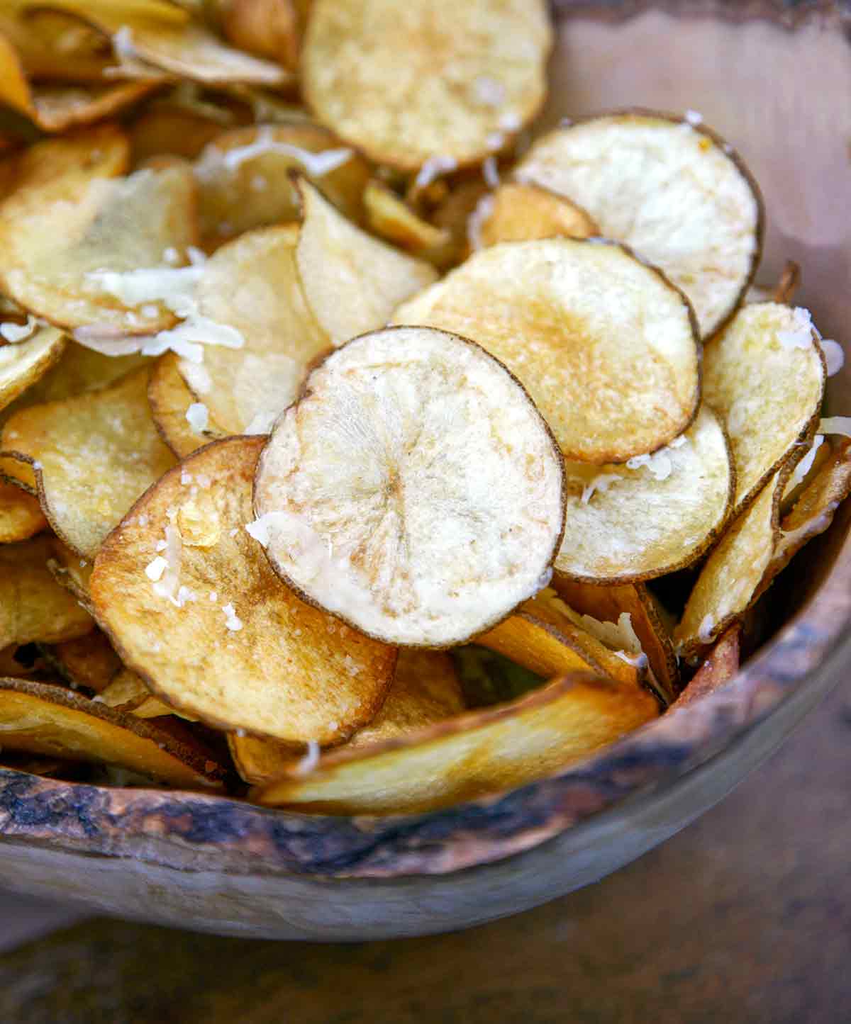 A wooden bowl filled with Manchego potato chips and sprinkled with more Manchego cheese.