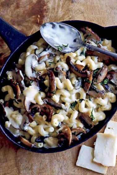 An oval skillet filled with mushroom macaroni and cheese with a spoon resting on top.