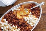 A white casserole dish filled with gingersnap and sweet potato casserole, topped with mini marshmallows and a spoon resting inside.