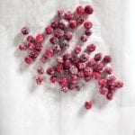Several sugared cranberries scattered across a sheet of parchment.