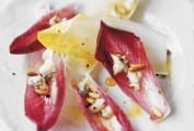 Leaves of endive salad with gorgonzola, pine nuts, and honey scattered on a white plate.