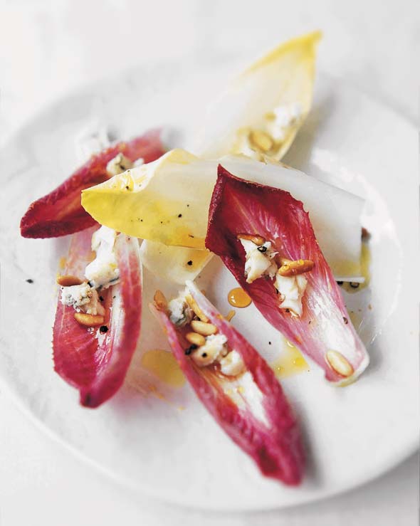 Leaves of endive salad with gorgonzola, pine nuts, and honey scattered on a white plate.