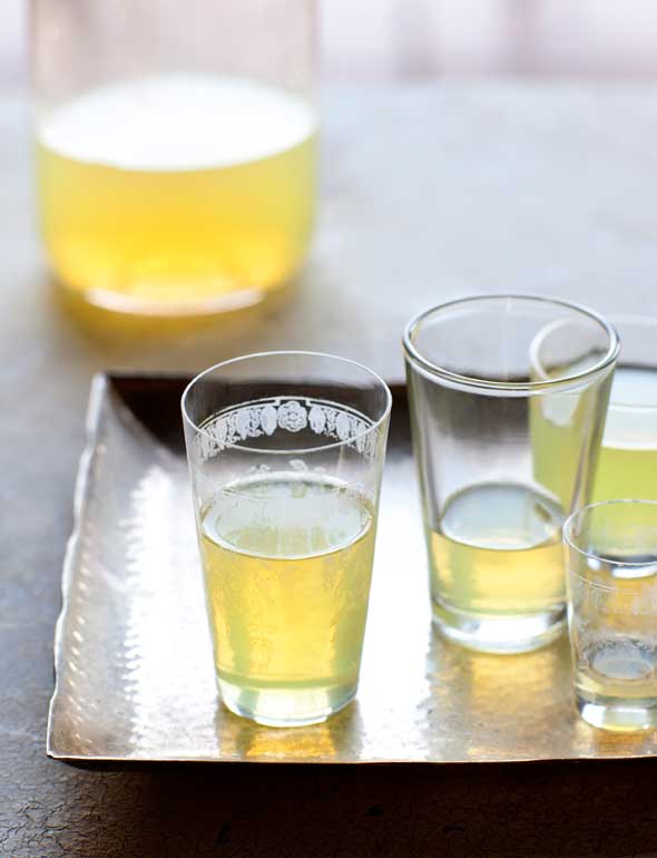 Several glasses partially filled with limoncello on a silver platter, with a bottle of limoncello in the background.