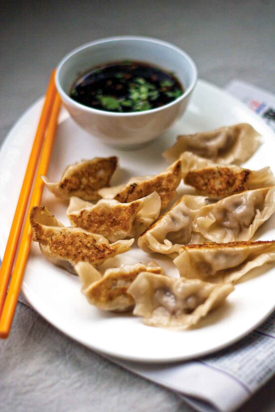 A white oval plate filled with pot stickers, a pair of chopsticks, and dipping sauce.