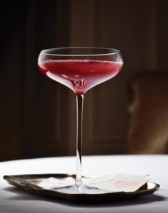 Blood orange and prosecco cocktail, in a coupe glass, on a small tray.