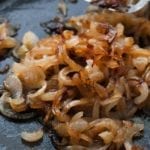 A skillet with caramelized onions and a spatula moving the onions.