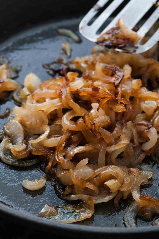 A skillet with caramelized onions and a spatula moving the onions.