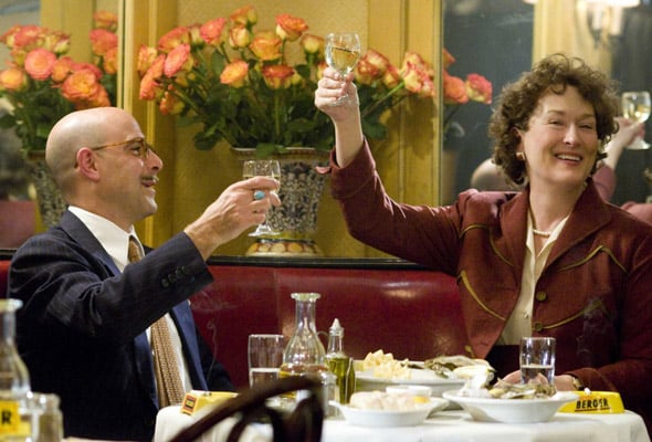 Julie and Julia toasting with wine glasses raised above a table in a restaurant.