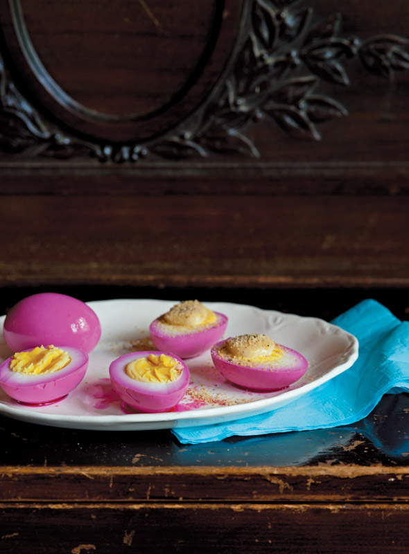 A plate of pink pickled eggs, cut in half and smeared with spiced mayonnaise