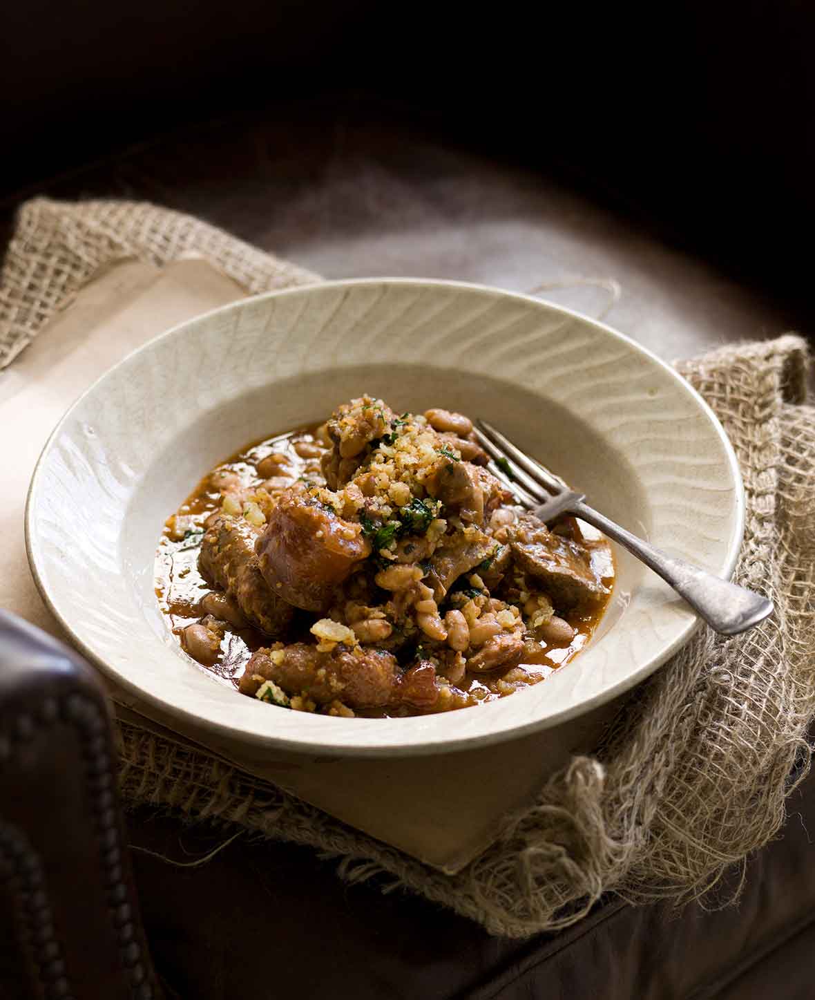 A white porcelain bowl filled with cassoulet and a fork rests on the side.