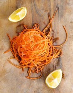 A grated carrot salad piled on a wooden cutting board with two lemon wedges.
