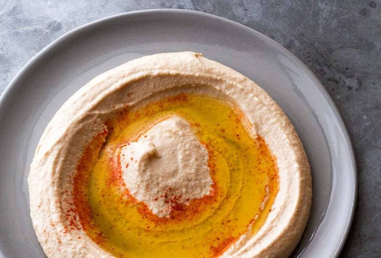 Homemade hummus sprinkled with paprika and drizzled with oil swirled on a grey plate.