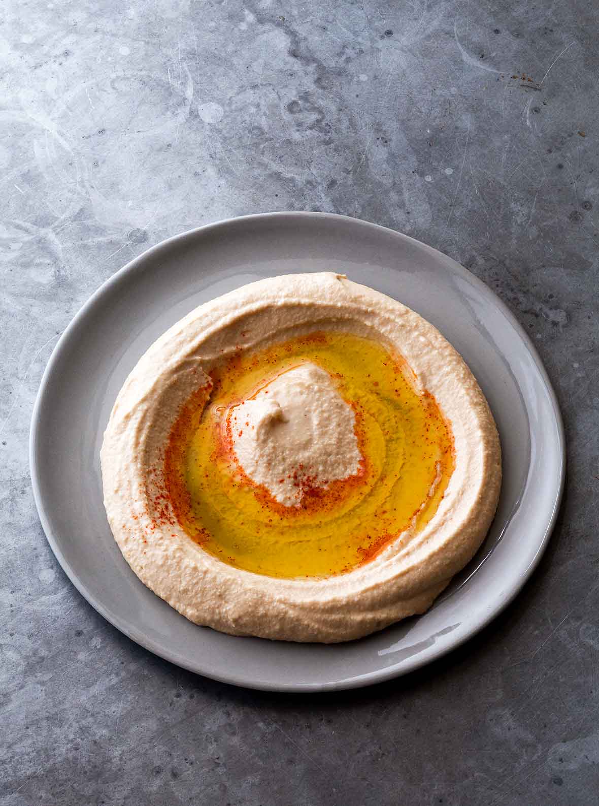 Homemade hummus sprinkled with paprika and drizzled with oil swirled on a grey plate.