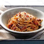 A big bowl of pasta swirled into a tomato-guanciale sauce in a simple bowl.