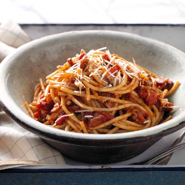 A big bowl of pasta swirled into a tomato-guanciale sauce in a simple bowl.