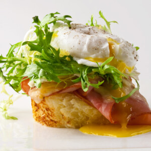 A single croque frisée on a white background with a little puddle of runny yolk.