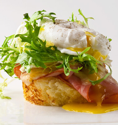 A single croque frisée on a white background with a little puddle of runny yolk.