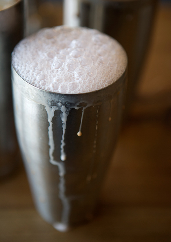 A metal shaker filled with a foamy egg cream.