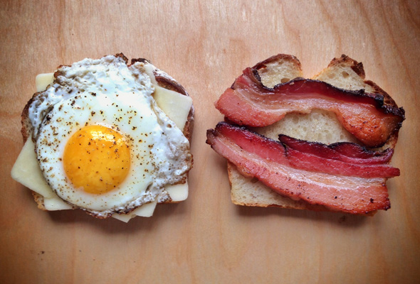 An egg on a slice of toast next to two bacon slices on a slice of toast.