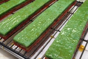 Brushing the warm apricot glaze on the strips of compressed rainbow cookie cakes.