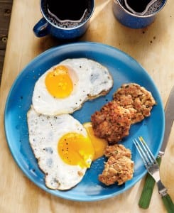 Three breakfast sausage patties on a blue plate with two fried eggs, bedside a cup of coffee.