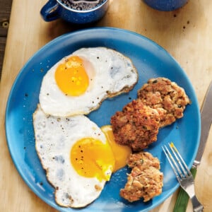 Three breakfast sausage patties on a blue plate with two fried eggs, bedside a cup of coffee.