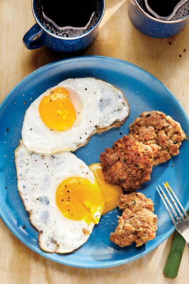 Three breakfast sausage patties on a blue plate with two fried eggs, bedside a cup of coffee.
